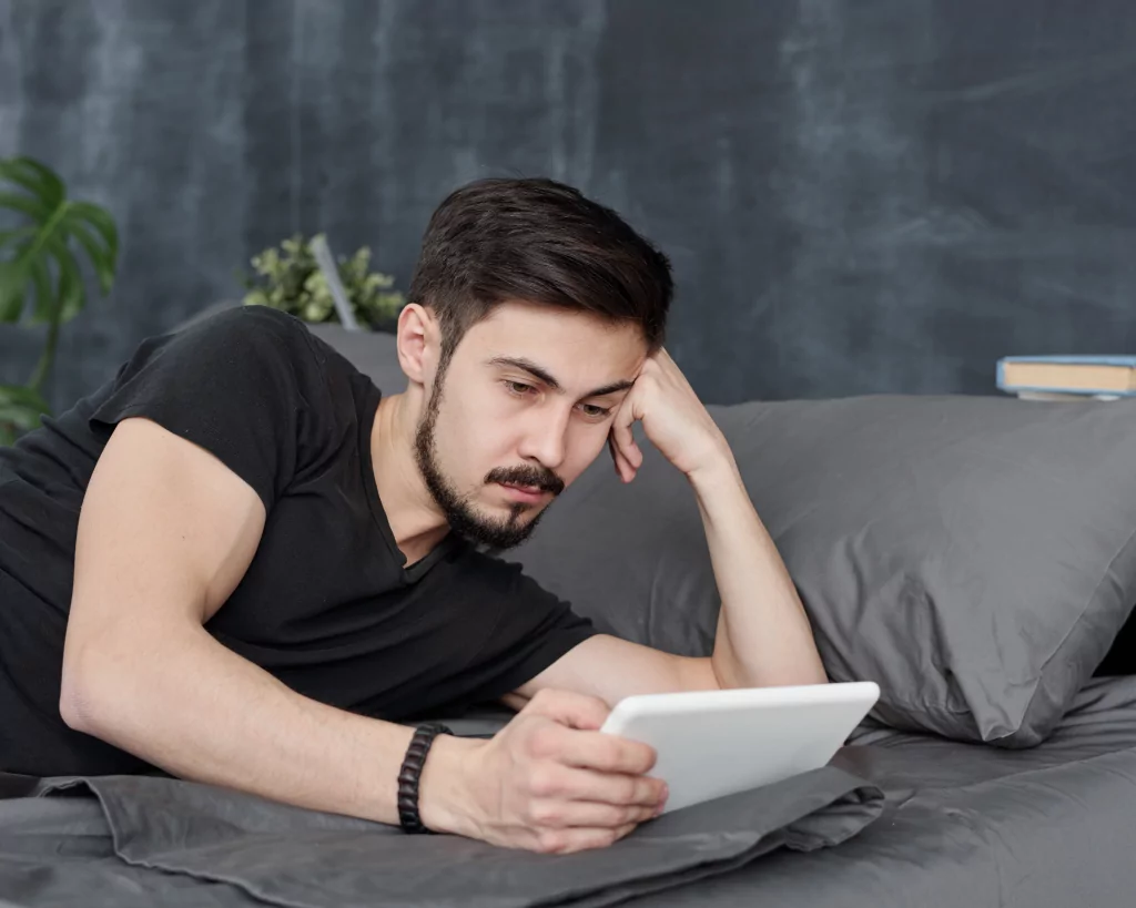 jeune homme installé allongé sur un canapé en train de regarder sa tablette et de perdre son temps